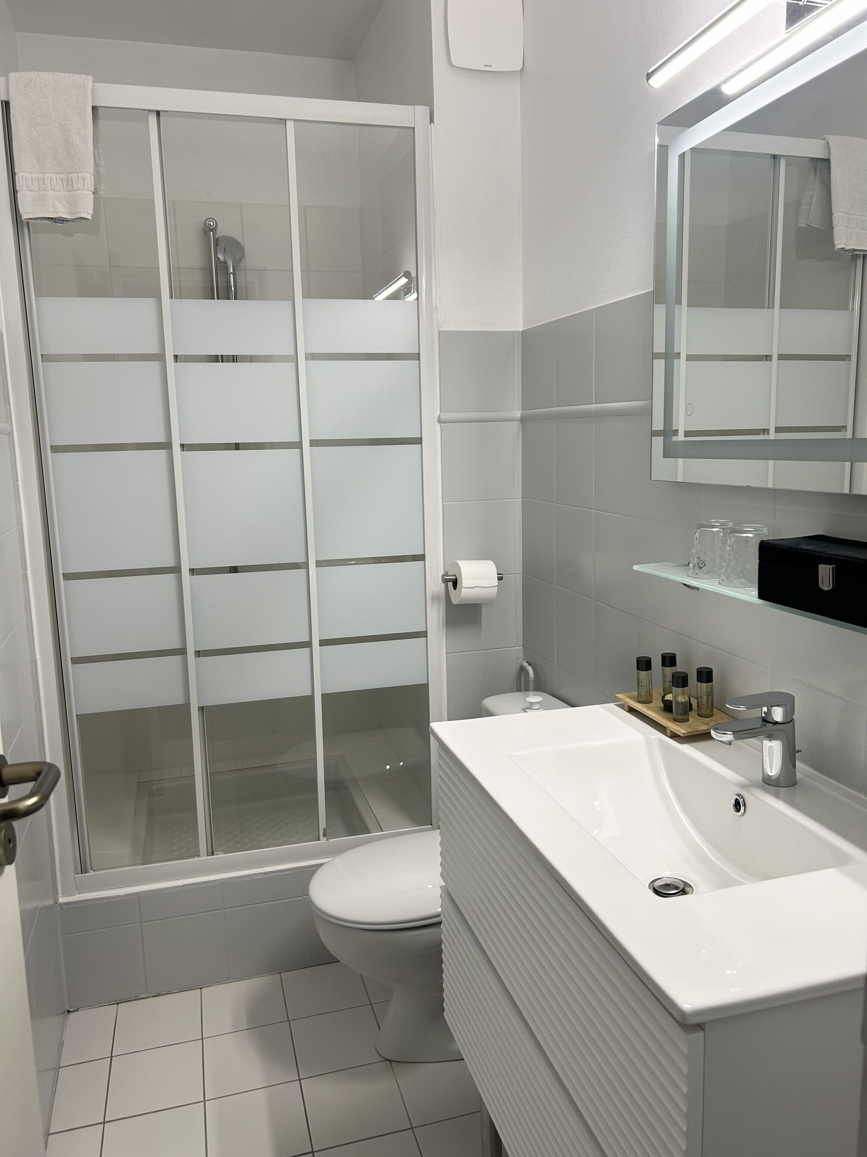A modern bathroom with a glass shower enclosure, a white sink with a vanity, and a mirror above the sink.