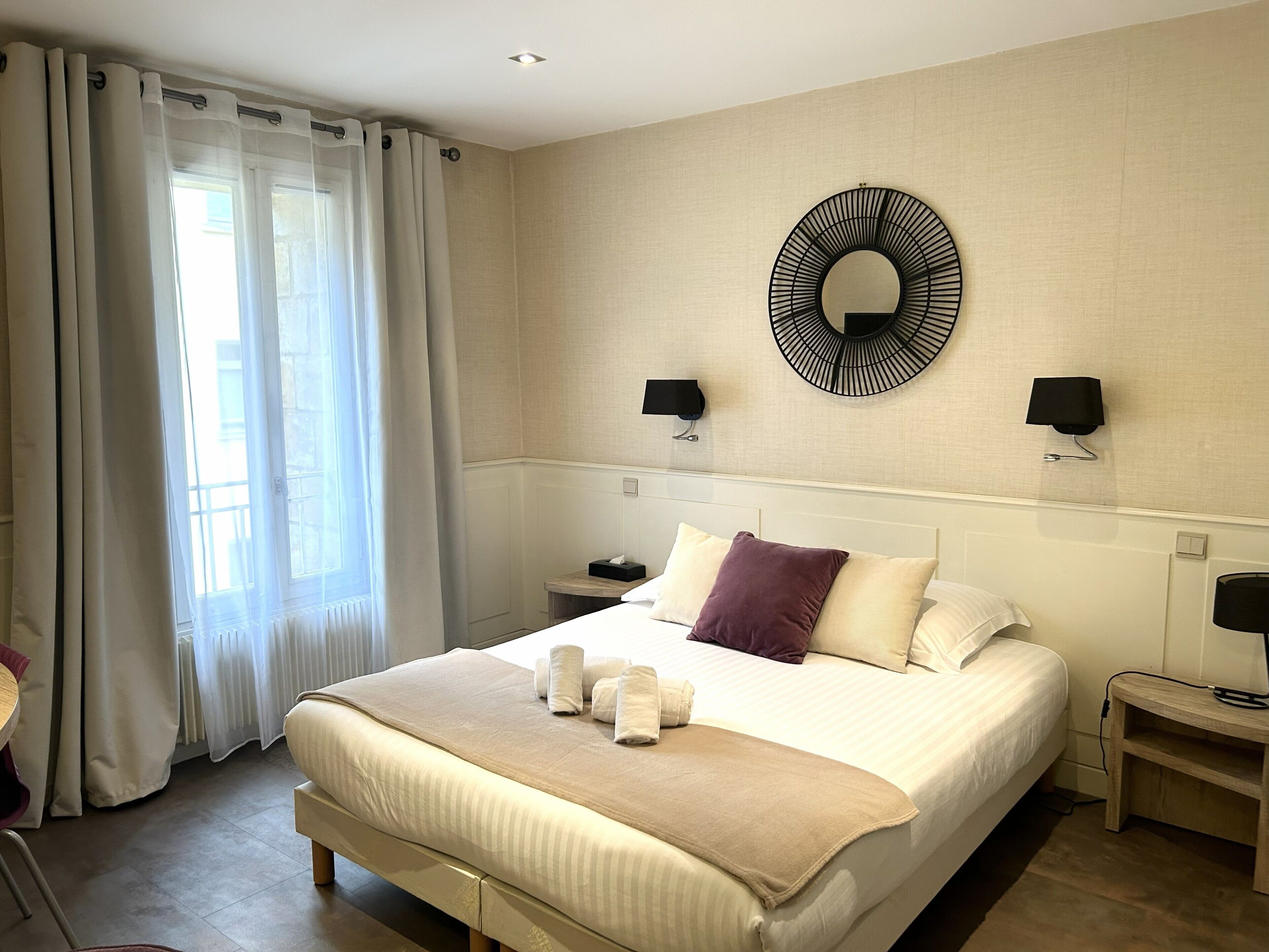Ein Hotelzimmer mit einem großen Bett, zwei Nachttischen, einem Wandspiegel und einem Fenster mit Vorhängen.