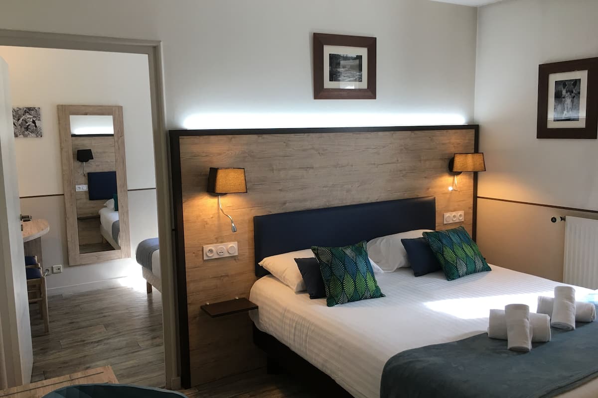 A hotel room with a large bed, two bedside lamps, a wooden headboard, a small bedside table, a mirror, and a framed picture on the wall.