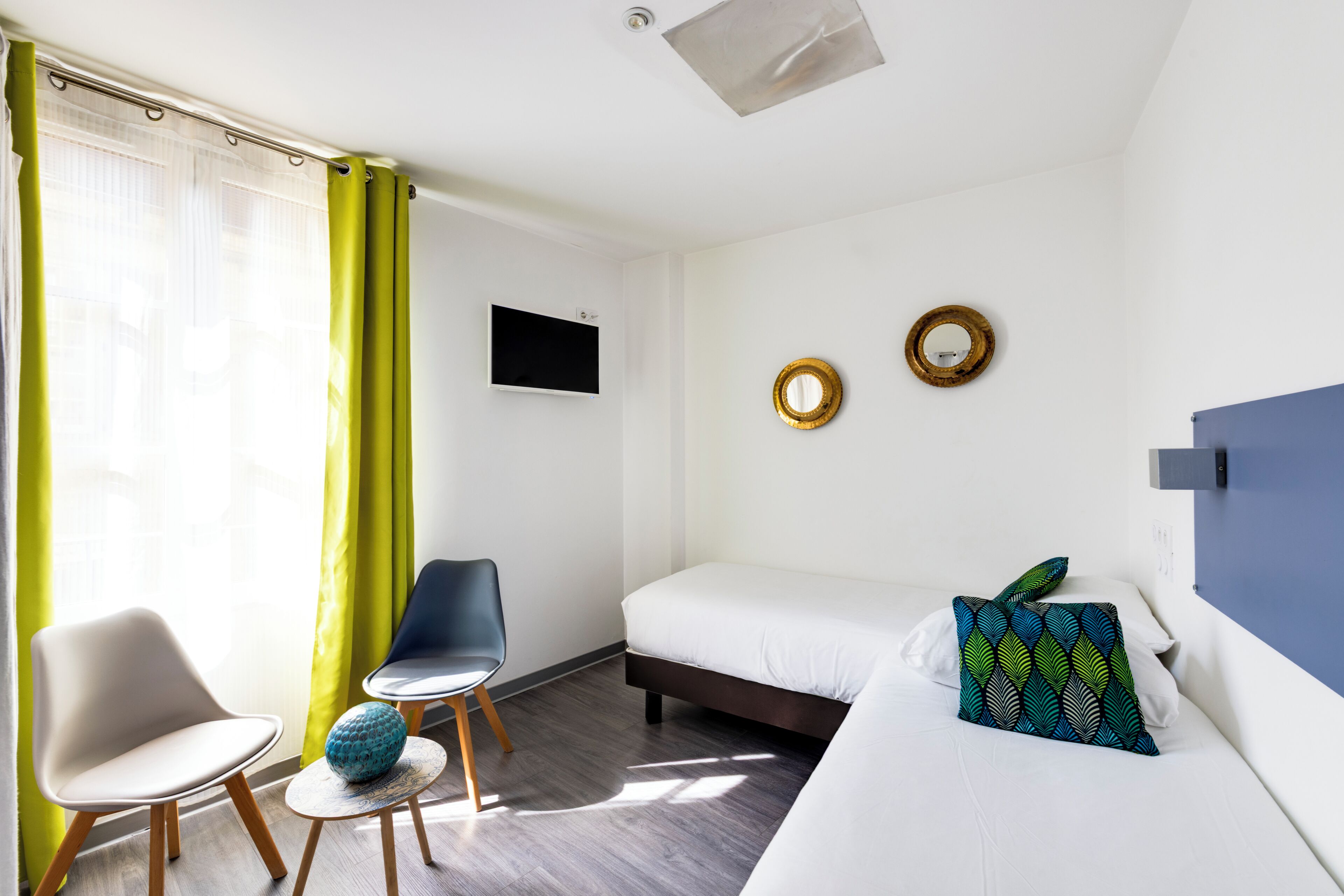 Ein Hotelzimmer mit einem Bett, einem Sessel, einem kleinen Tisch, einem Fernseher und zwei Wandspiegeln.