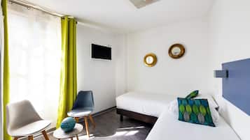 Une chambre d’hôtel équipée d’un lit, d’une chaise, d’une petite table, d’un téléviseur et de deux miroirs fixés au mur.