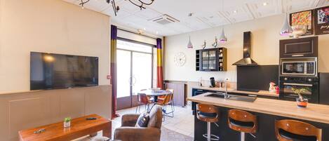 Una cocina moderna con una isla central, taburetes de bar, un área de comedor con mesa y sillas, y un televisor montado en la pared.