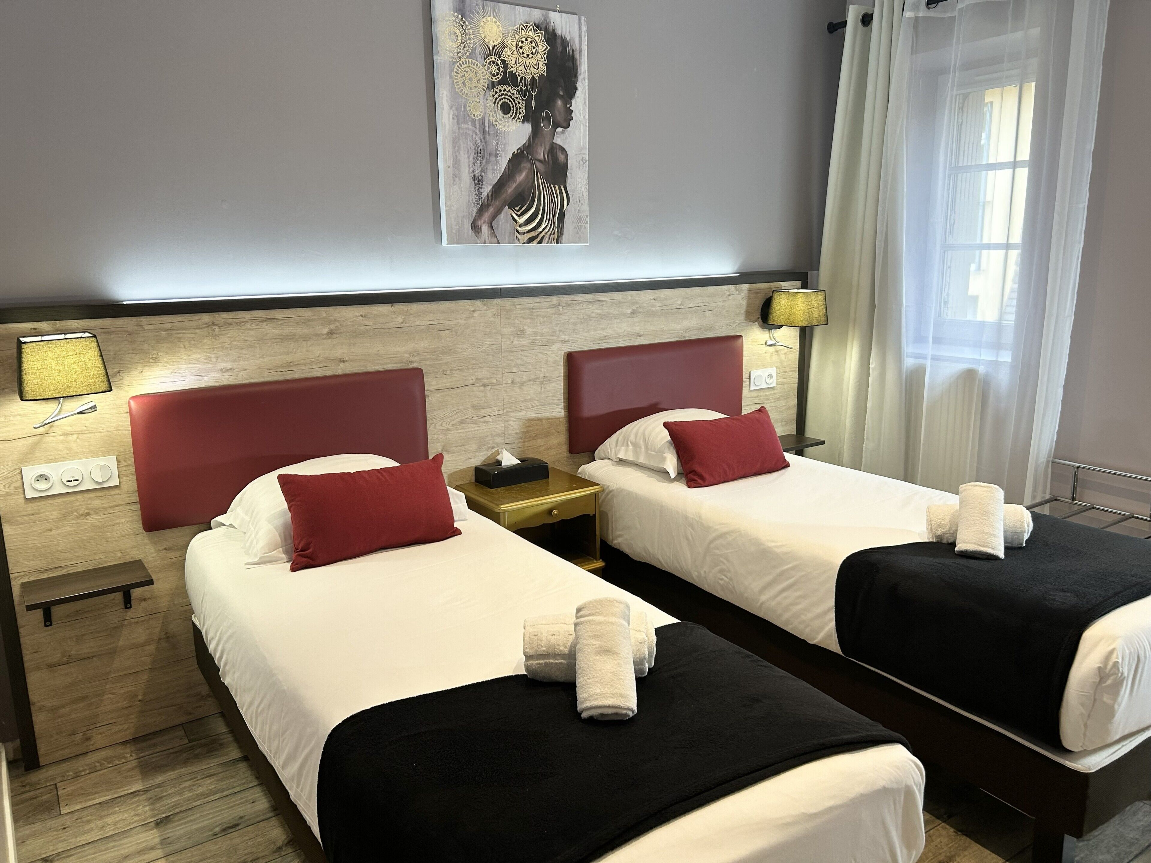 Une chambre d’hôtel avec deux lits, une table de chevet, une lampe, un tableau au mur et une fenêtre avec des rideaux.