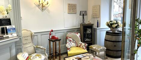 A cozy room with a vintage telephone, a patterned armchair, a small table with magazines, and a decorative lamp.
