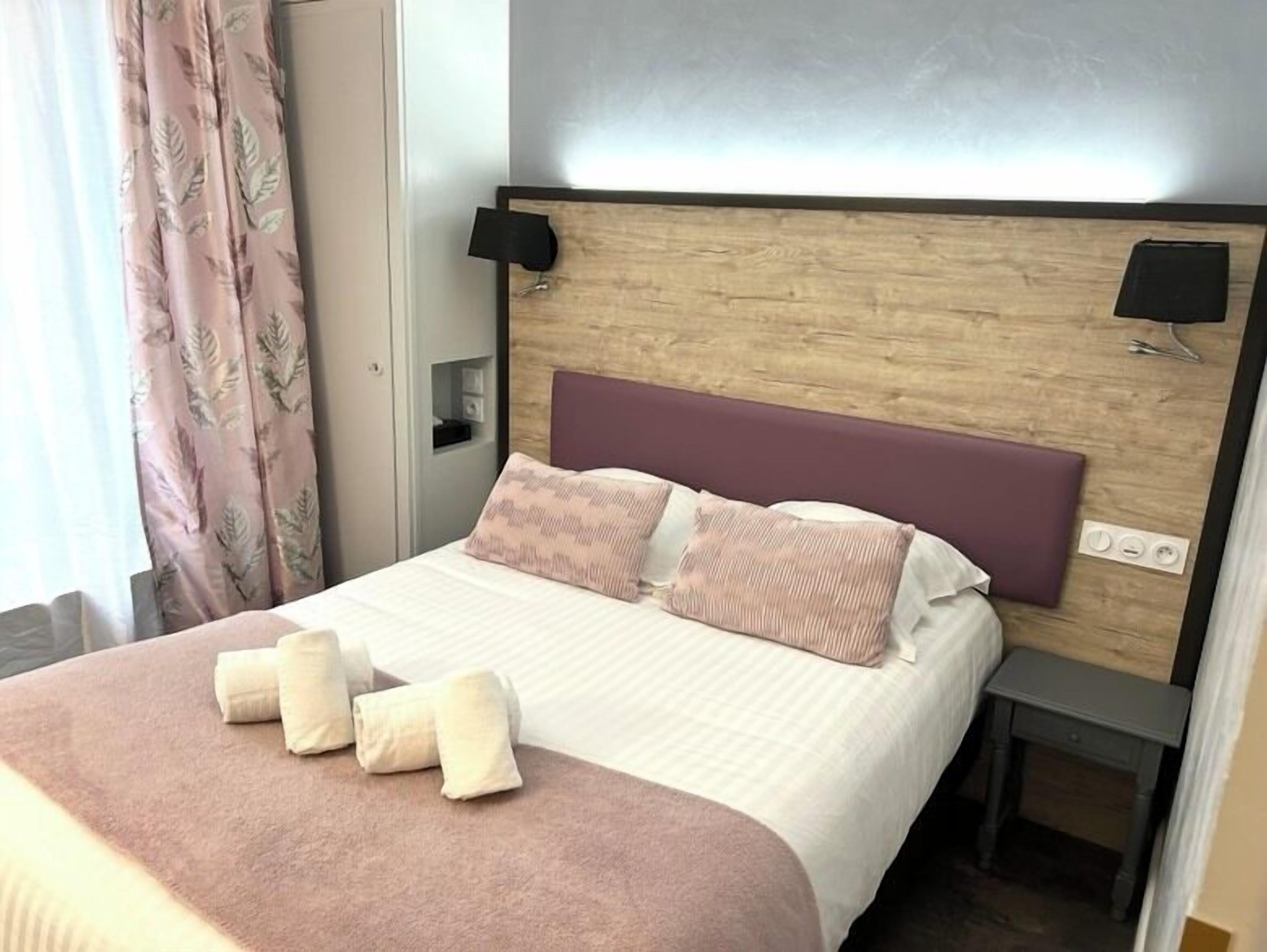 A hotel room with a bed, a nightstand, and a wall-mounted lamp.