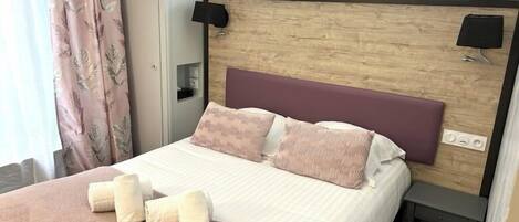 A hotel room with a bed, a nightstand, and a wall-mounted lamp.