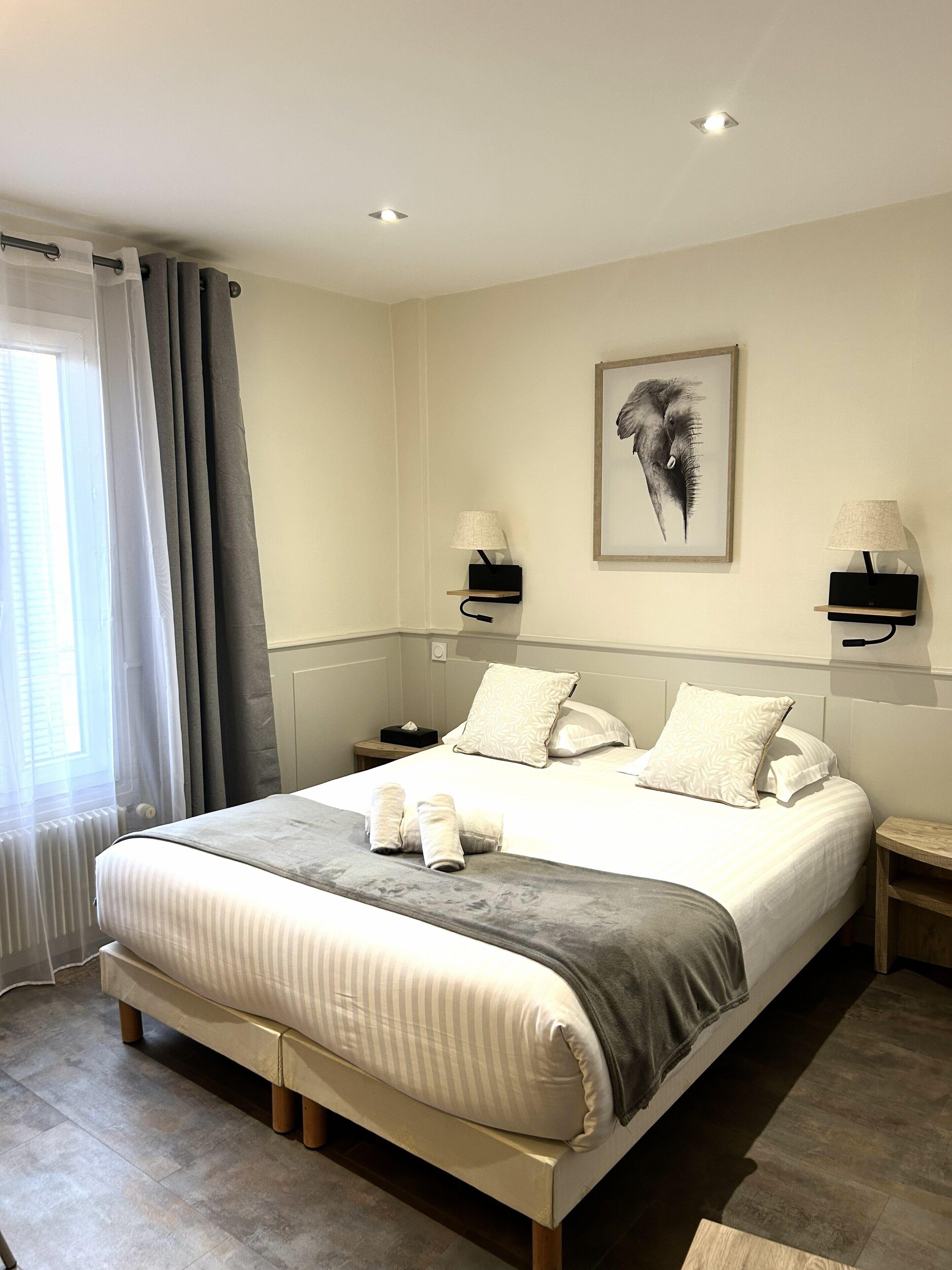 A modern bedroom with a large bed, two bedside tables, a wall-mounted lamp, and a framed picture.