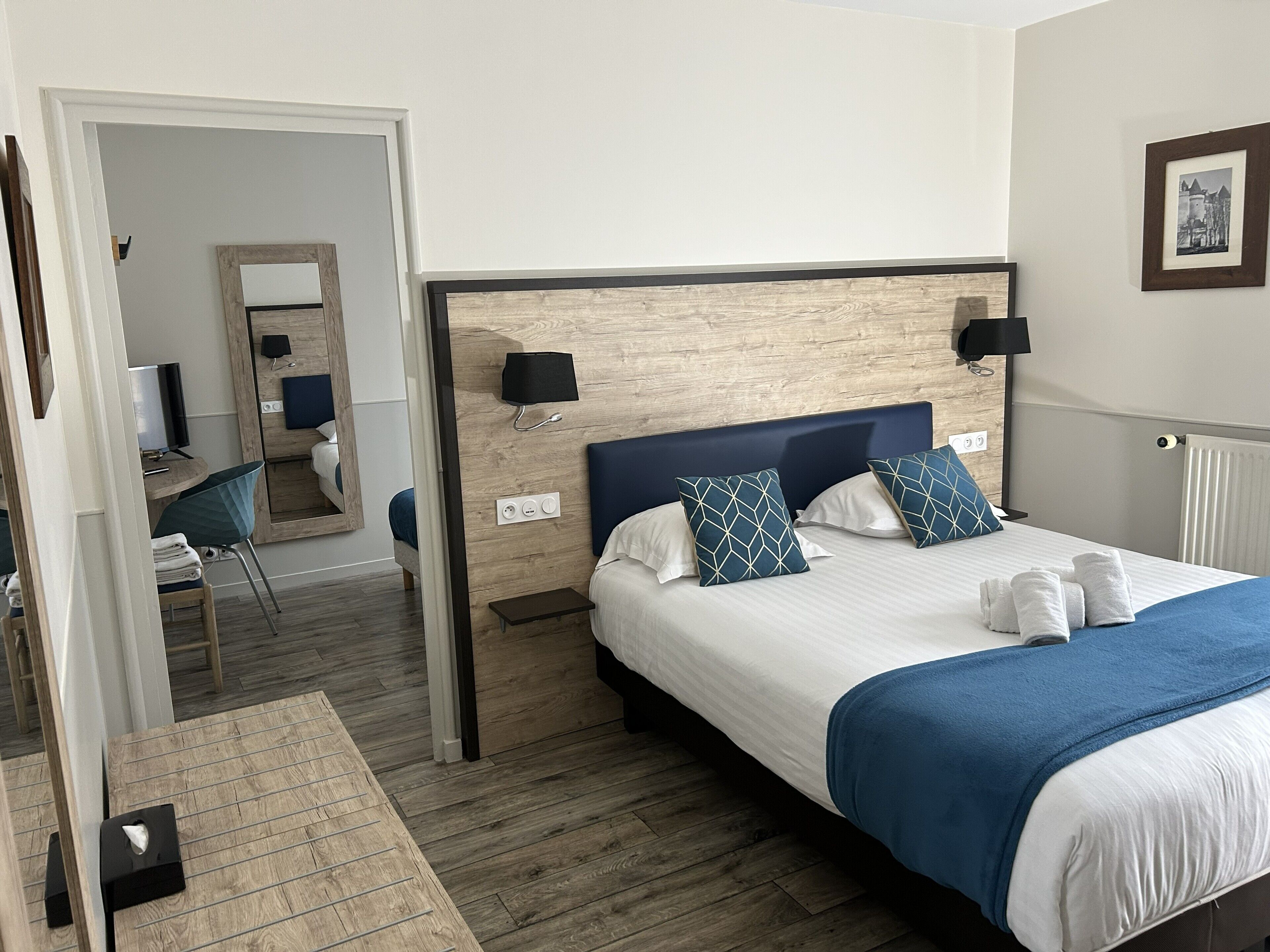 Ein Hotelzimmer mit Bett, Nachttischlampen, einem Schreibtisch mit Stuhl, einem Spiegel und einer Heizung.