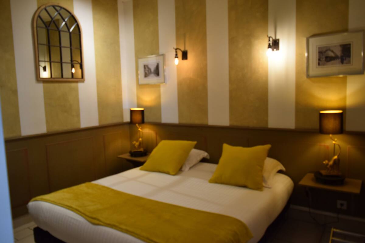 A hotel room with a large bed, two bedside lamps, a window, and a wall-mounted picture.