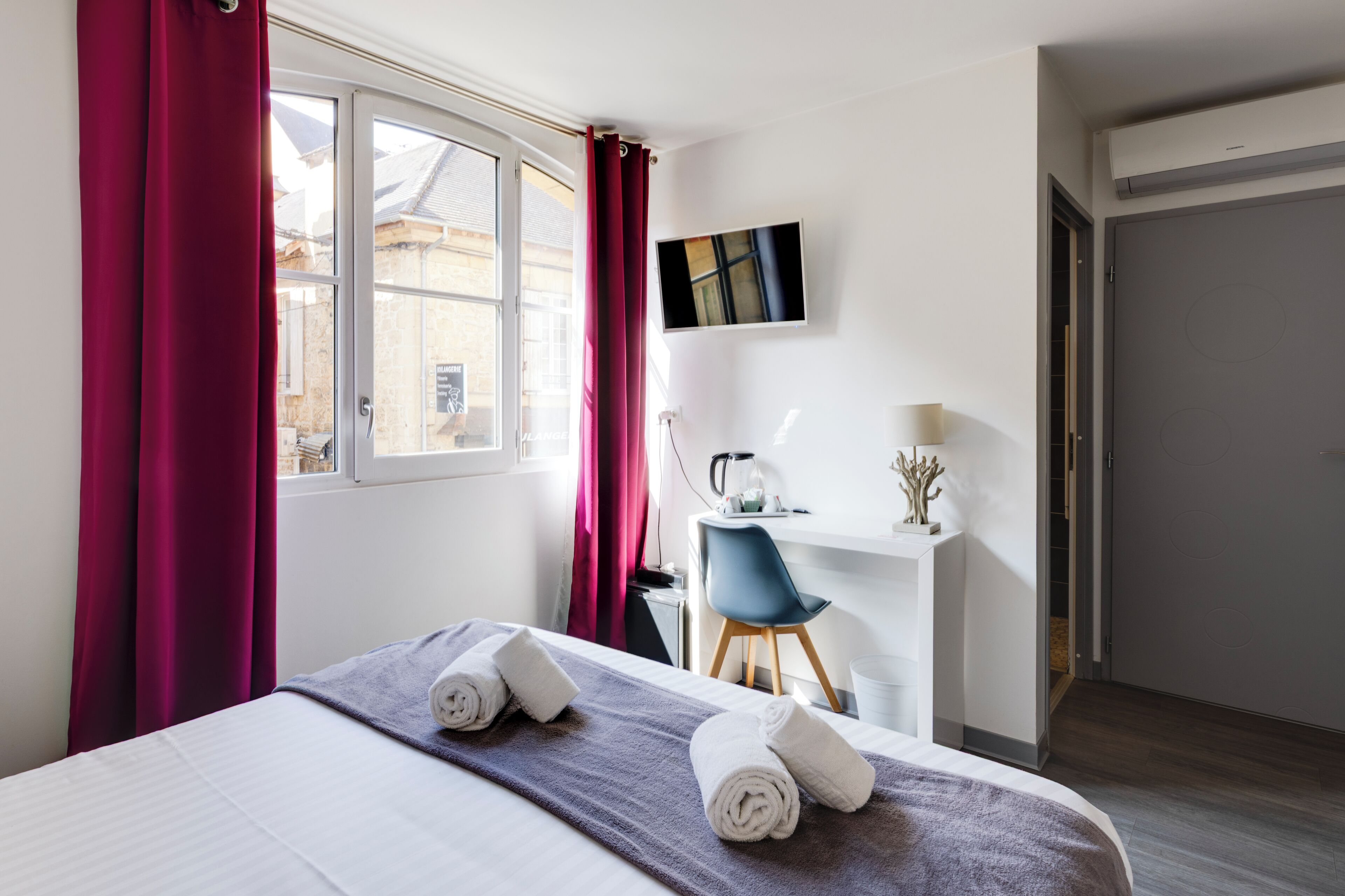 Une chambre d’hôtel avec un lit, un bureau, une chaise et un téléviseur fixé au mur.