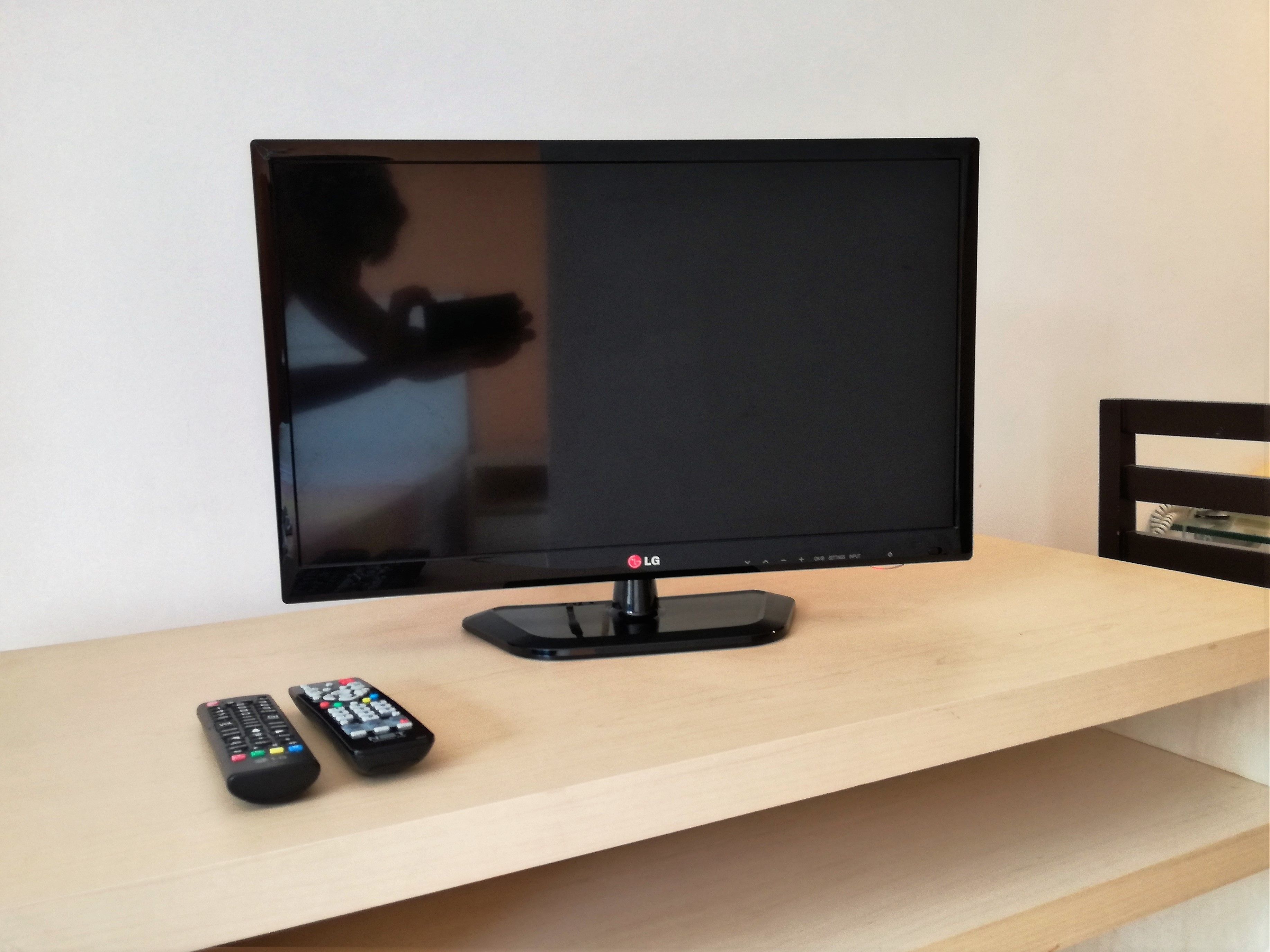 A flat-screen TV on a wooden TV stand with two remote controls.