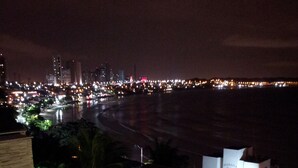 A nighttime view of a hotel with a swimming pool, outdoor seating, and a view of the beach and city lights. - Aparthotel Margherita (Natal)