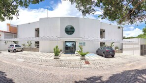A modern building with a circular skylight, a covered entrance, and potted plants. - Aparthotel Margherita (Natal)