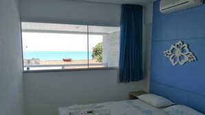 A bedroom with a bed, a window with a view of the sea, a blue wall, and a decorative wall piece. - Aparthotel Margherita (Natal)
