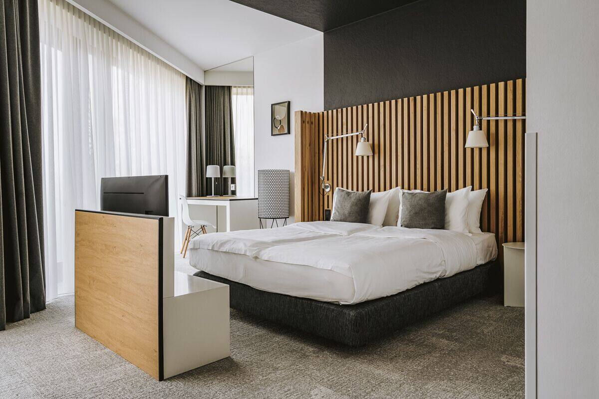 Ein modernes Hotelzimmer mit einem großen Bett, einem Schreibtisch, einem Sessel und einem Fernseher.