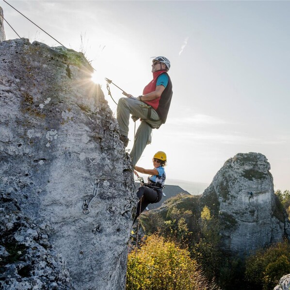 Una persona haciendo rappel por un risco rocoso, usando arnés y cuerdas.