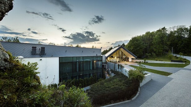 A modern building with large glass windows, a sloped roof, and a pathway leading to a wooden structure. - Poziom 511 Jura Wellness Hotel & Spa (Ogrodzieniec)