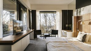 A modern hotel room with a large bed, a desk with a TV, and a view of trees through the window. - Poziom 511 Jura Wellness Hotel & Spa (Ogrodzieniec)
