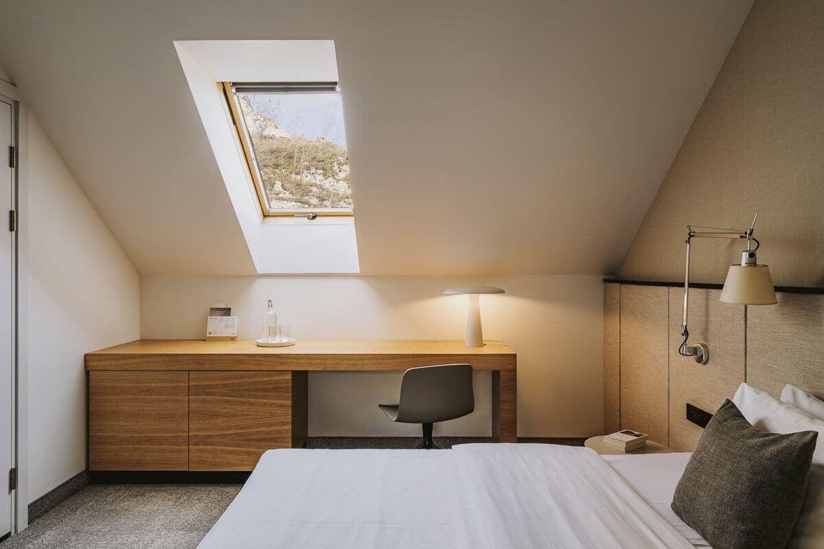 Ein Schlafzimmer mit Dachfenster, Schreibtisch, Stuhl, Bett und Nachttisch.
