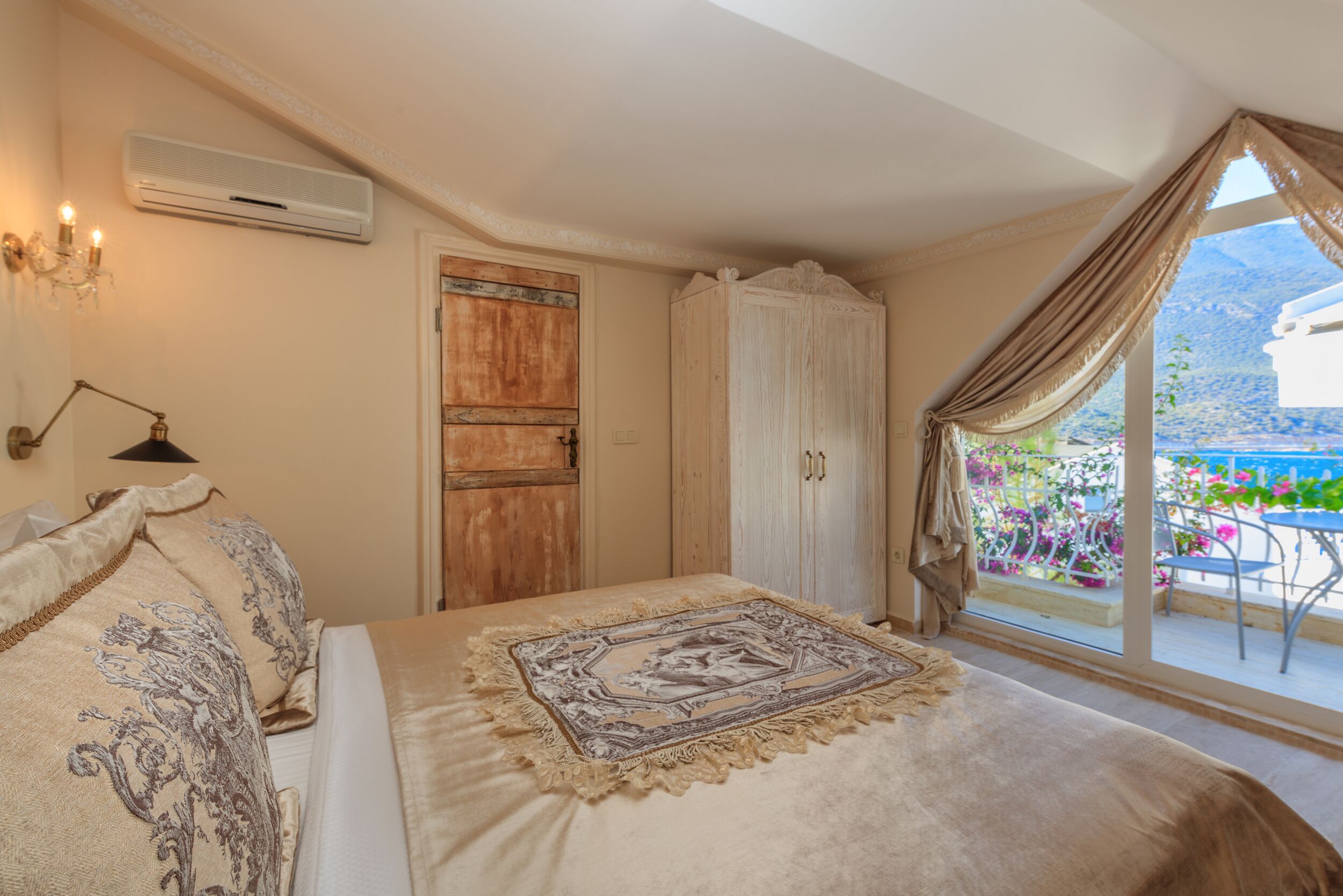 Een slaapkamer met een groot bed, een houten garderobe, een raam met gordijnen en een balkon met bloemen.