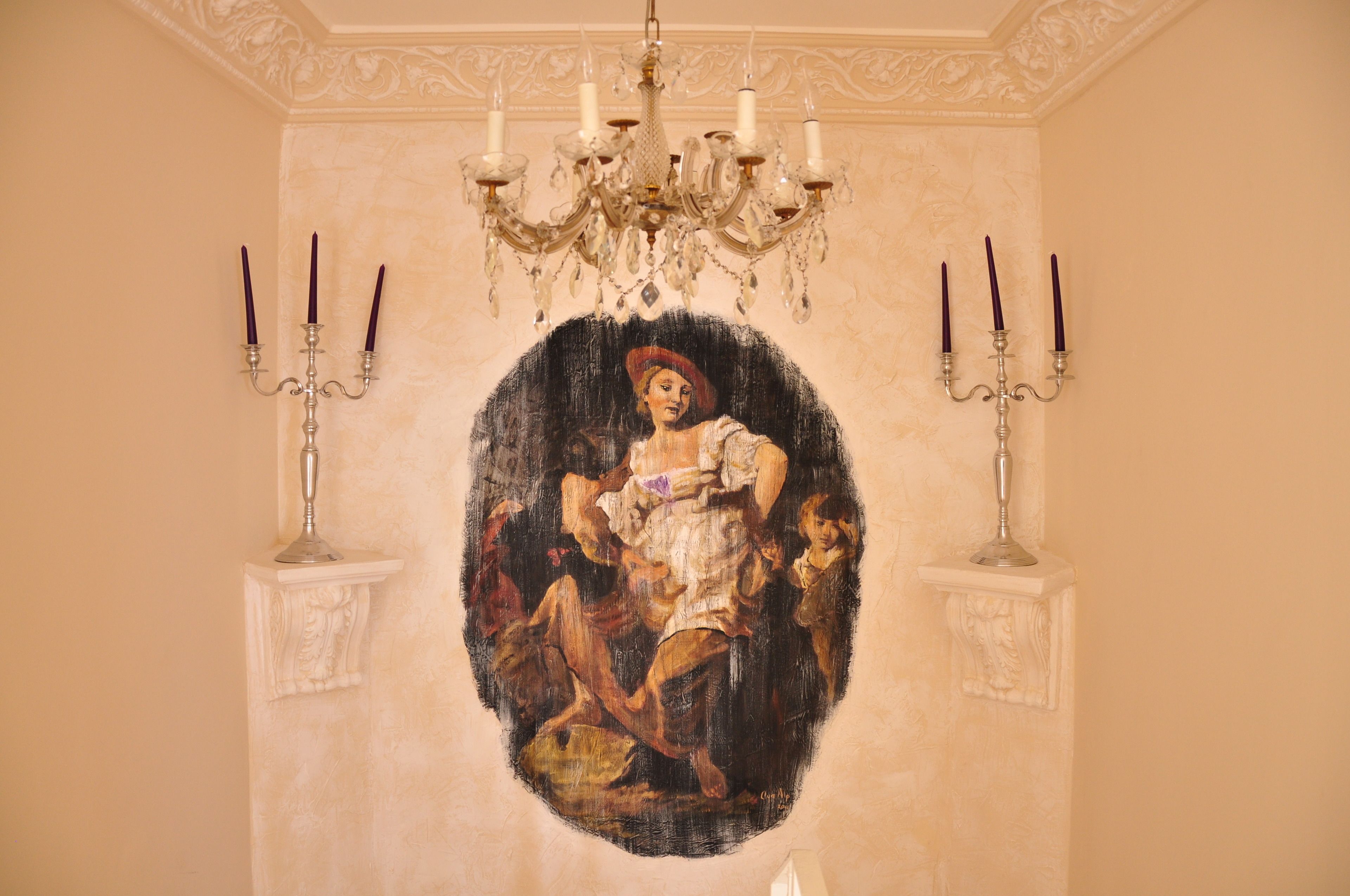Una habitación con un cuadro ovalado grande en la pared, una araña y candelabros.