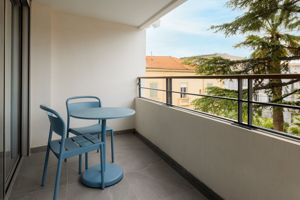 A balcony with a table and chairs, a view of buildings and trees, and a railing.
