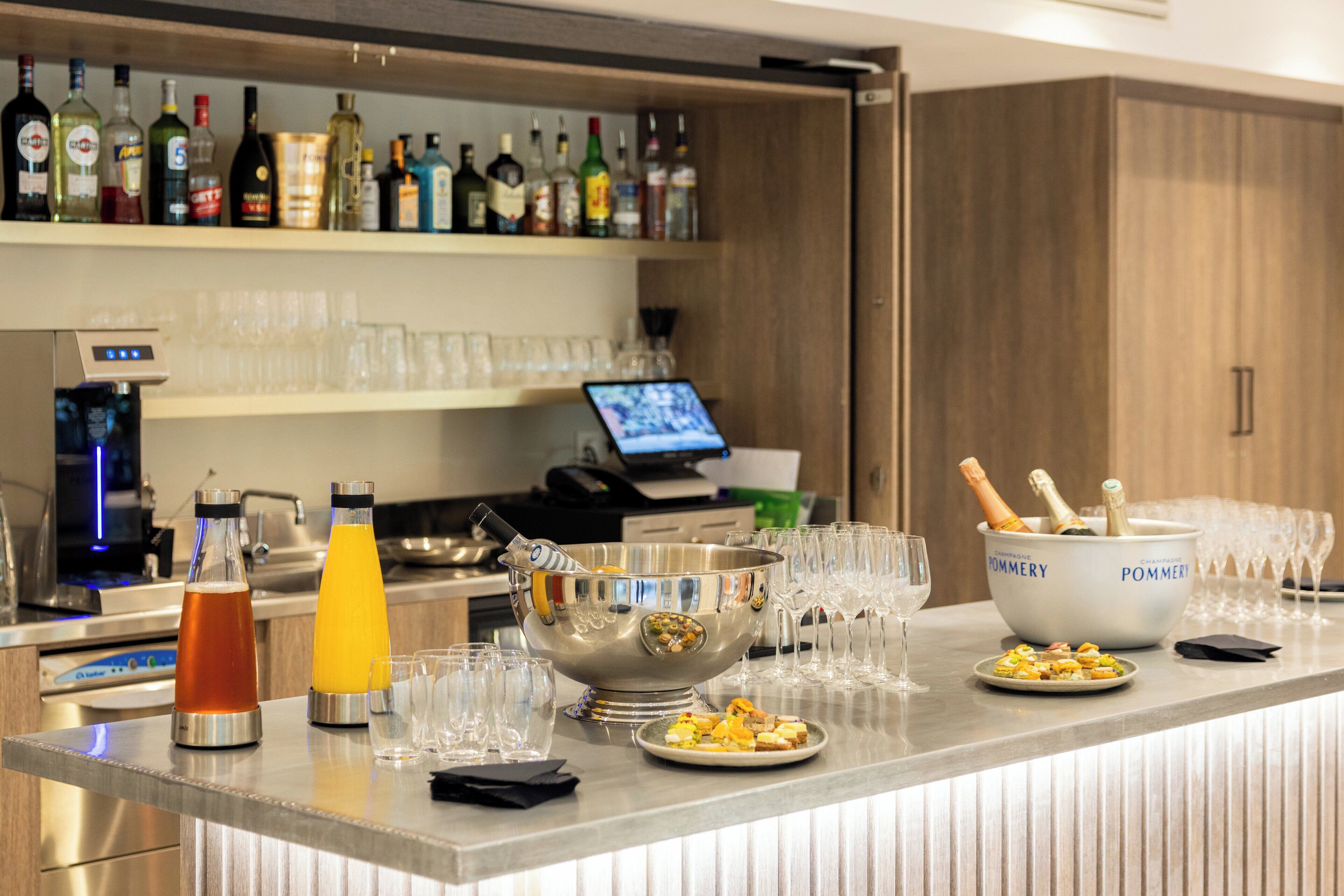 A bar area with a variety of liquor bottles, a cocktail shaker, glasses, and a bowl with champagne.