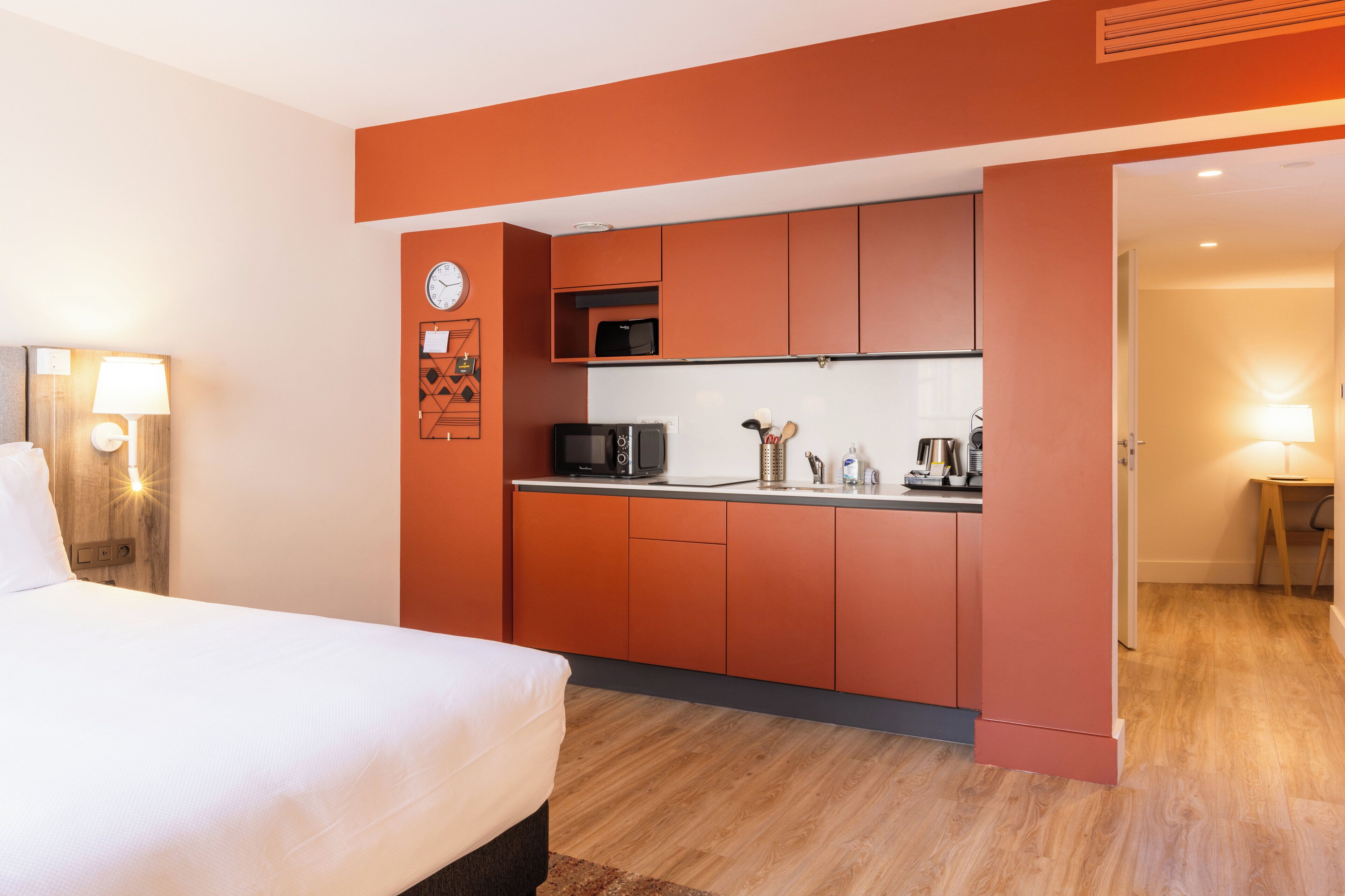 A compact hotel room with a bed, a kitchenette, and a small dining area.