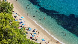 Una playa con agua turquesa cristalina, gente nadando y tomando el sol, y sombrillas en la arena.