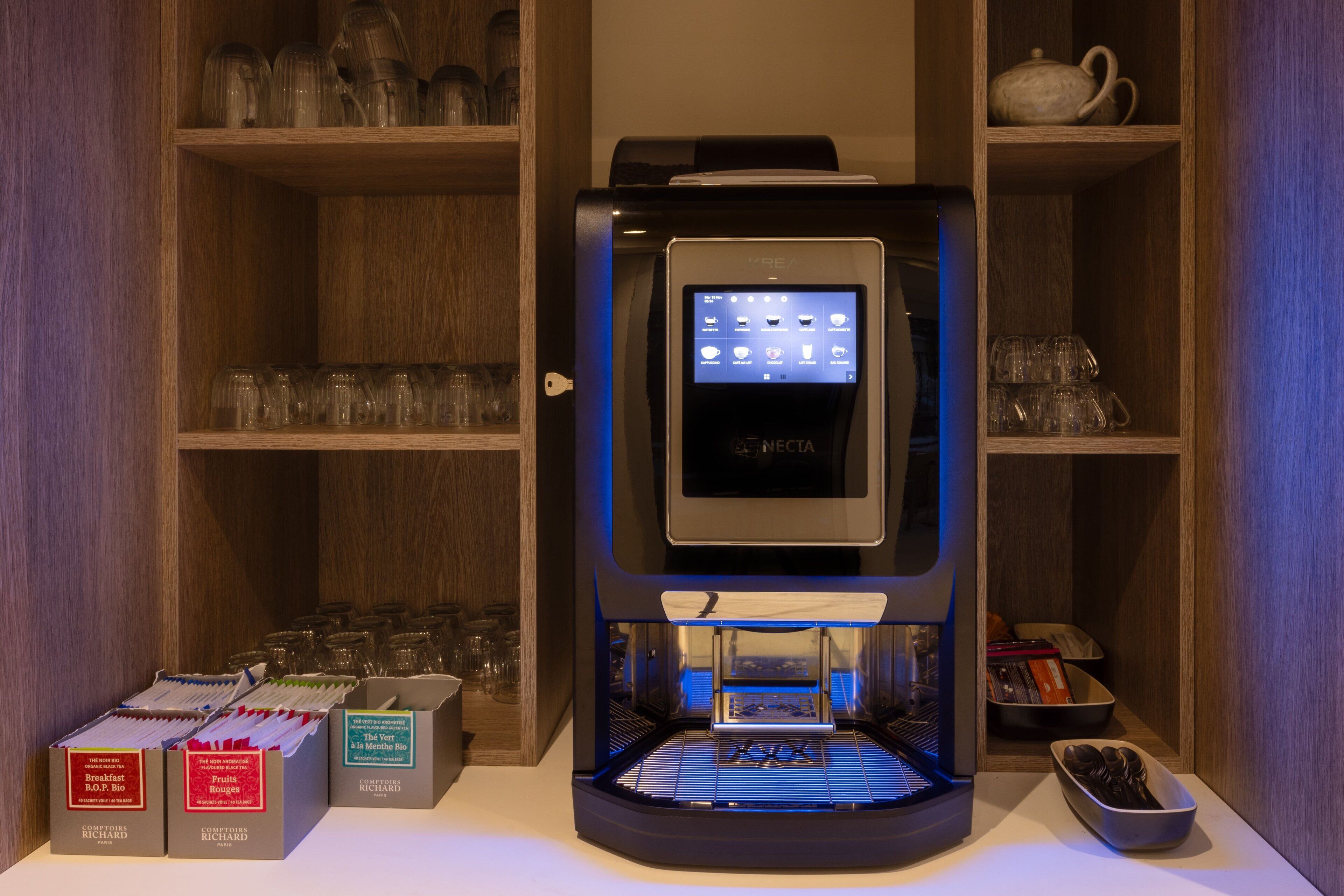 A coffee machine with a digital display, surrounded by shelves with glassware and boxes of coffee pods.