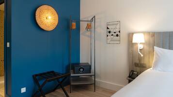 Une chambre d’hôtel avec un mur d’accent bleu, un lit avec une literie blanche, une table de chevet avec une lampe, un téléphone et une petite armoire.