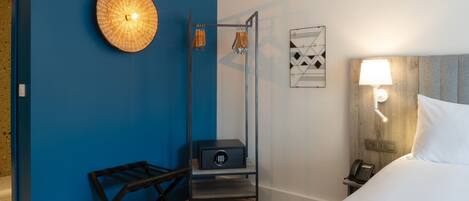 Une chambre d’hôtel avec un mur d’accent bleu, un lit avec une literie blanche, une table de chevet avec une lampe, un téléphone et une petite armoire.