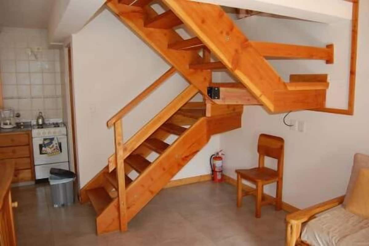 Une cuisine compacte avec un escalier en bois menant à une mezzanine.
