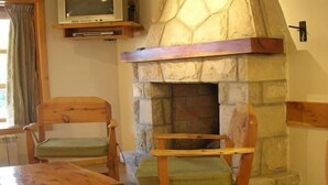 Una habitación acogedora con chimenea de piedra, sillas de madera, una mesa y una ventana con cortinas.