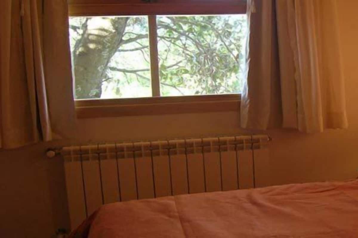 Une chambre à coucher avec un lit, une fenêtre avec des rideaux, un radiateur et une lampe de chevet.