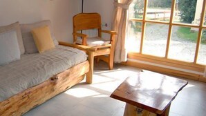 Un sofá de madera con cojines, una silla de madera y una mesita en una habitación con un ventanal grande.