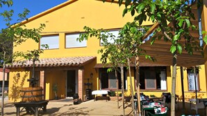 Un edificio amarillo con techo de tejas, una banca y mesas al aire libre con sillas.