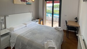 Habitación de hotel con una cama grande, un escritorio, una silla, un televisor y un balcón con vista al mar.