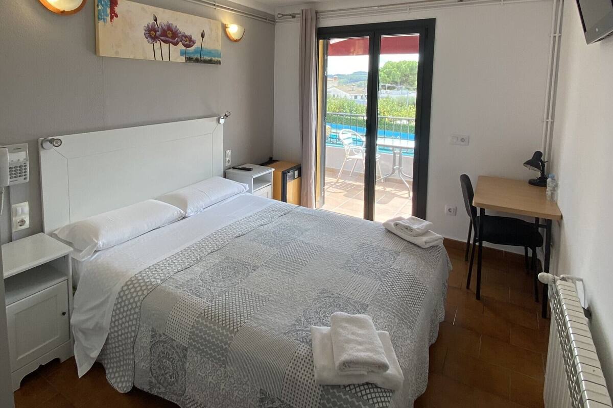 A hotel room with a large bed, a desk, a chair, a TV, and a balcony with a view of the sea.