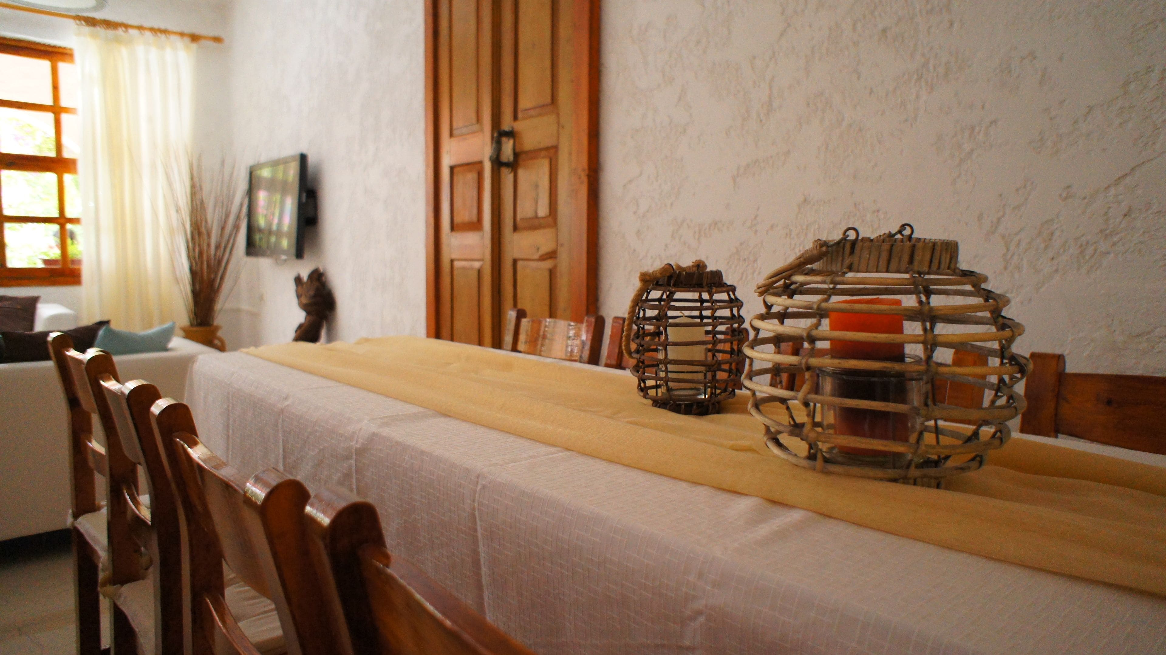 Uma mesa de jantar com toalha branca, cadeiras de madeira e dois castiçais.