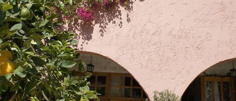 A multi-story building with a pink facade, balconies with plants, and a courtyard with outdoor seating.