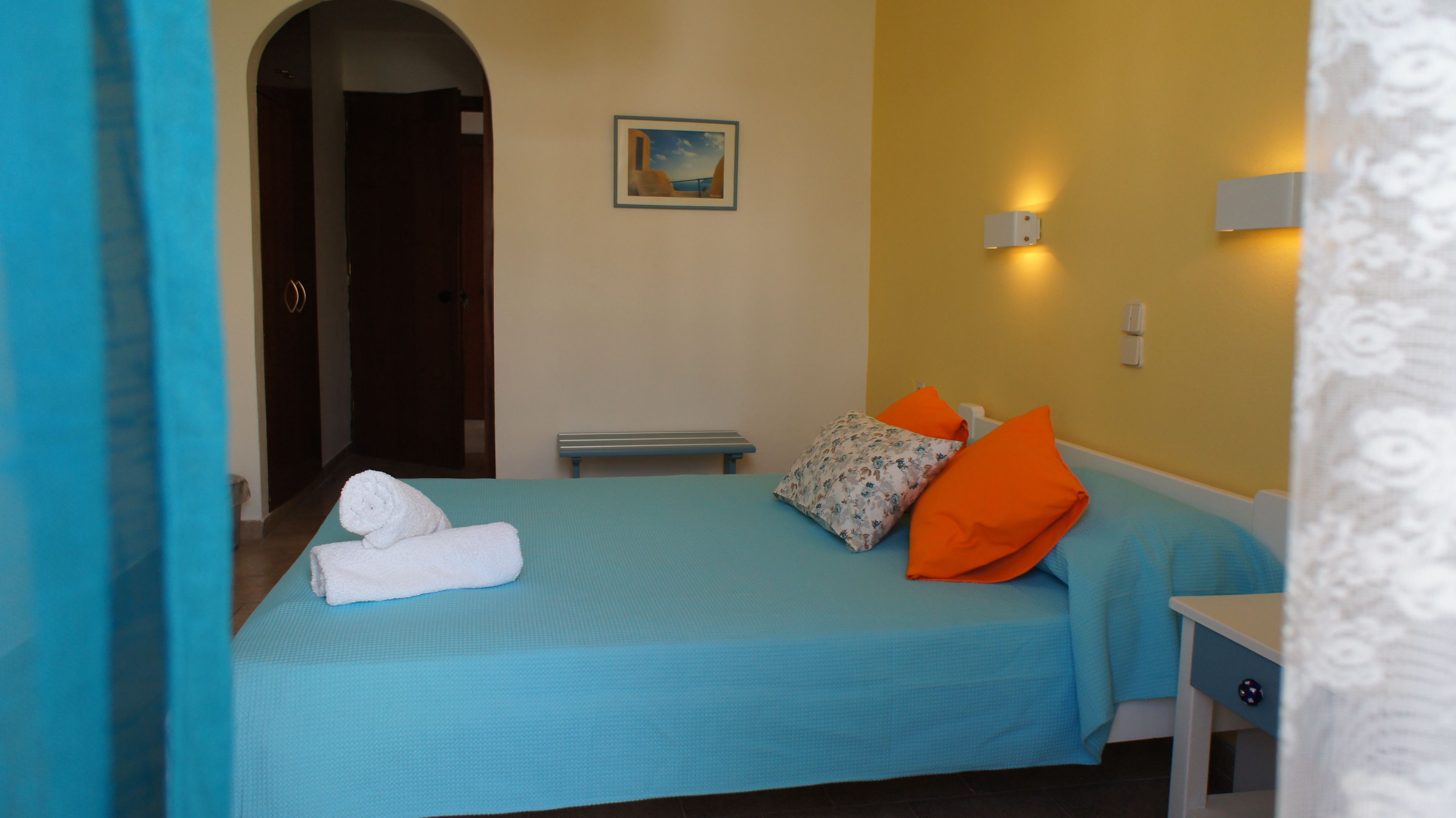 Ein Hotelzimmer mit einem Bett, einer Bank, einer Tür und einem Wandbild.