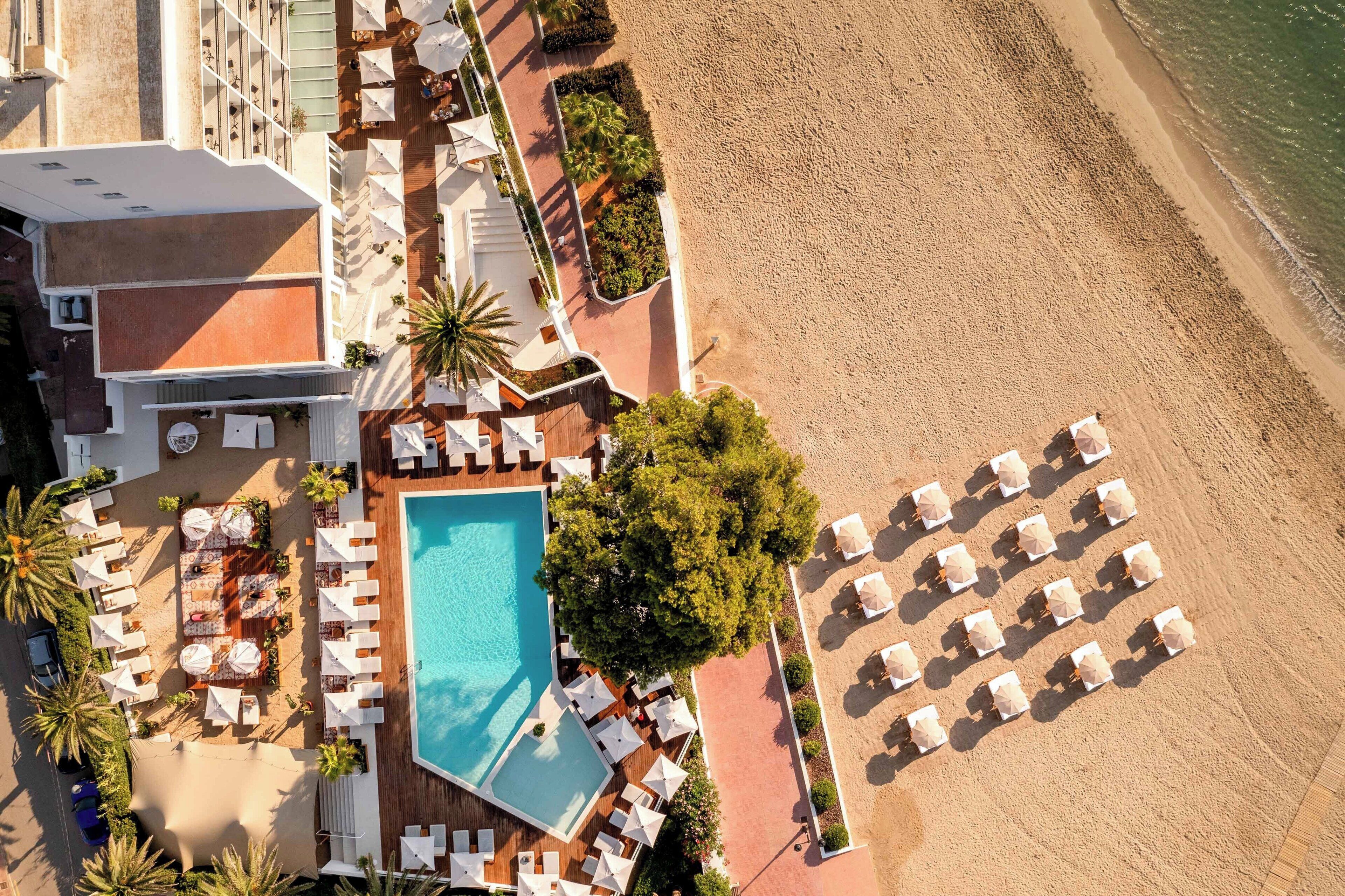 An aerial view of a resort with a swimming pool, sun loungers, and a beach area.