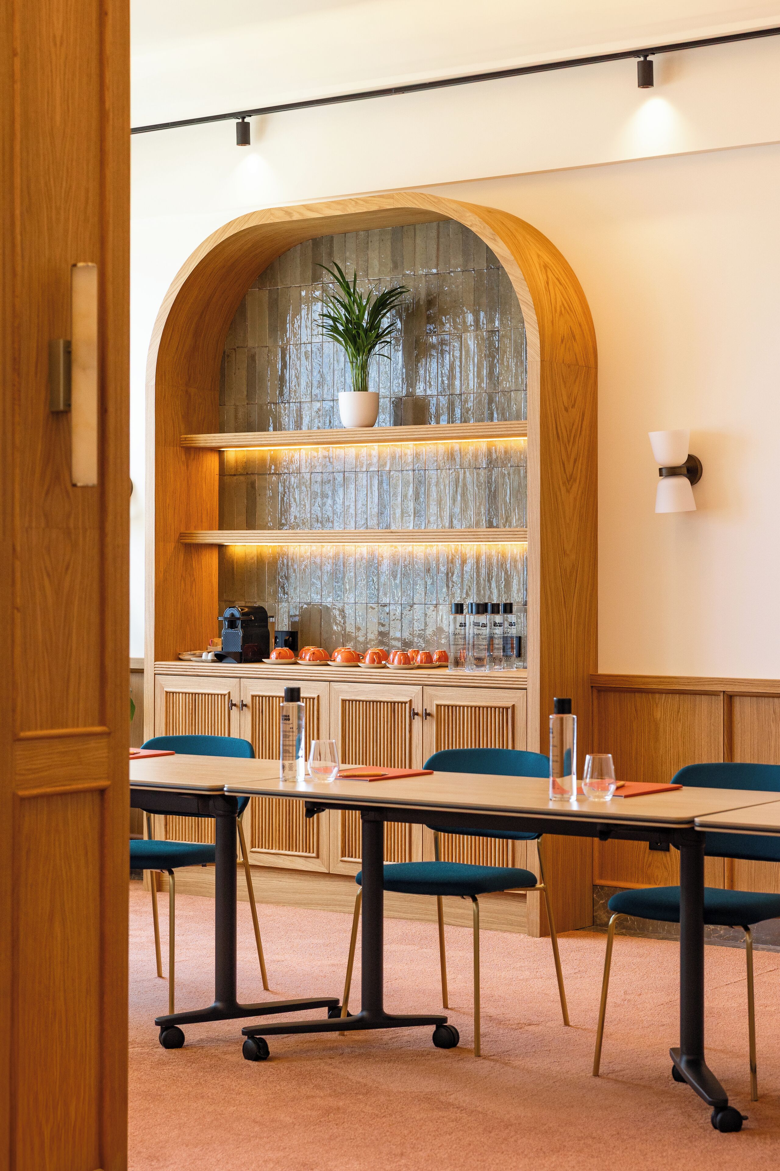 Un salón de conferencias con una mesa de madera, sillas azules y una zona de cocina al fondo.
