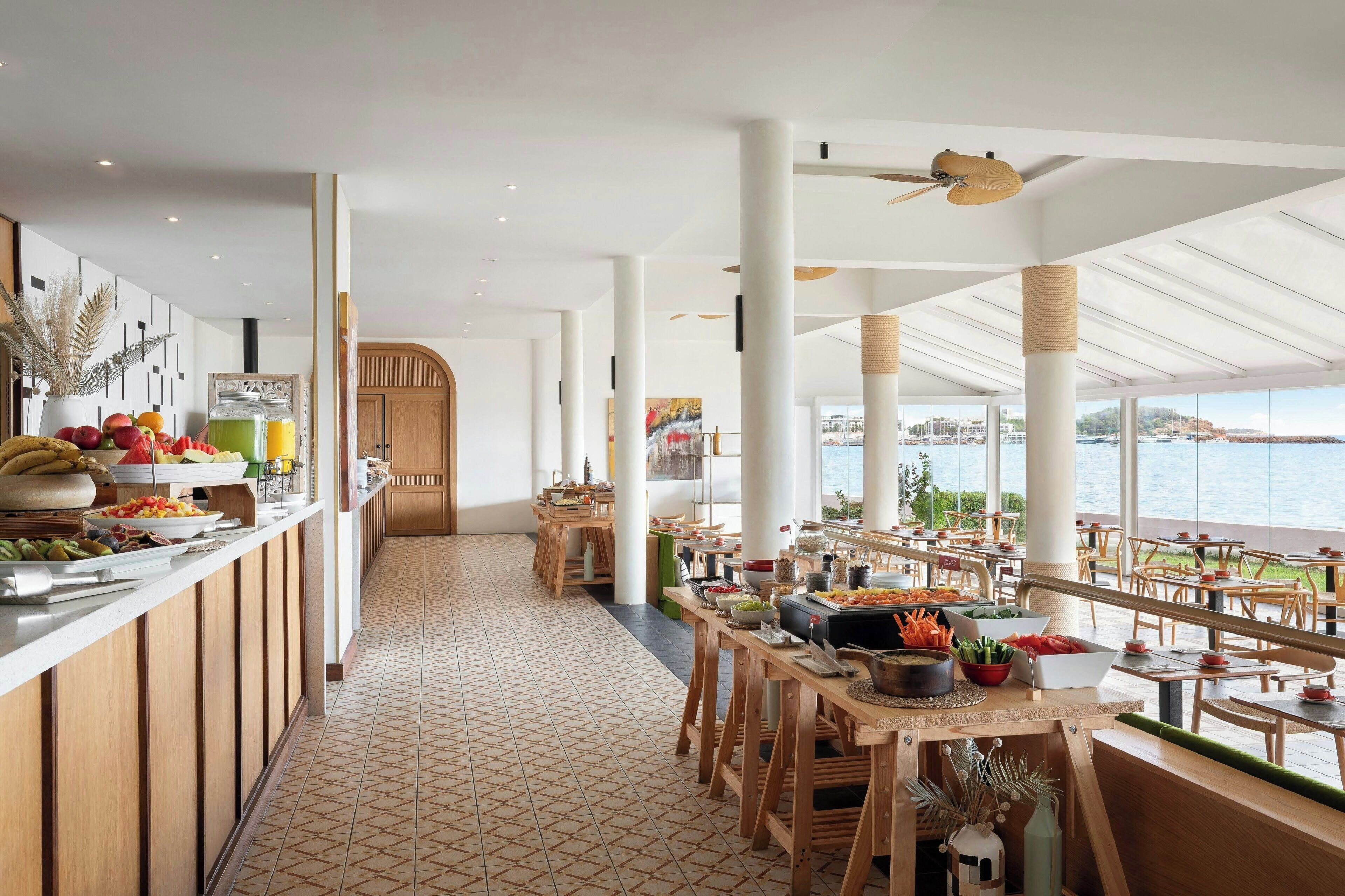 C’est un restaurant spacieux avec un long comptoir, des tables et des chaises en bois. Il offre une vue sur la mer et possède un sol carrelé.