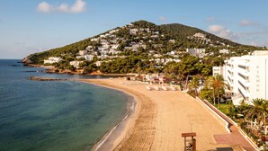 A beach with a sandy shore, a clear blue sea, and a hillside with buildings. - Hotel Riomar Ibiza, A Tribute Portfolio Hotel (Santa Eulalia del Rio)