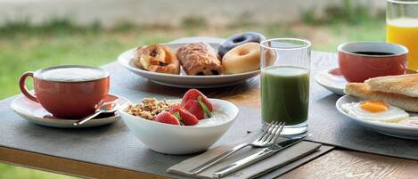 A breakfast table with various food items and a glass of orange juice, overlooking a beach.