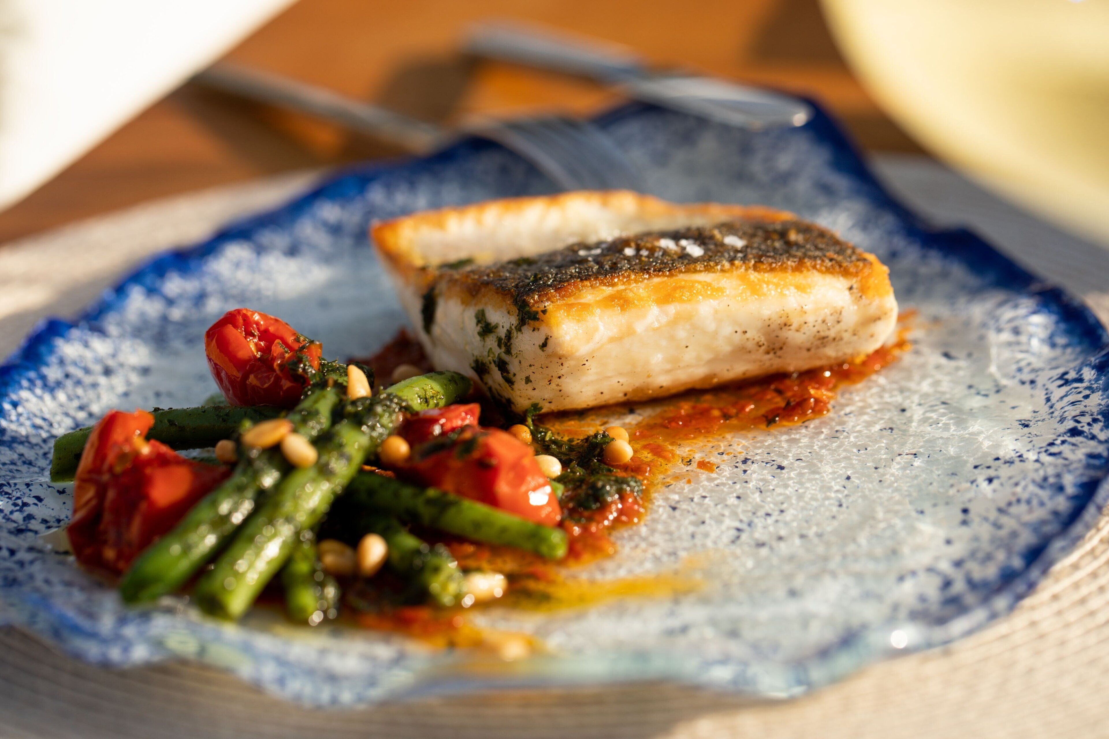 A plate with a piece of fish, green beans, and tomatoes.
