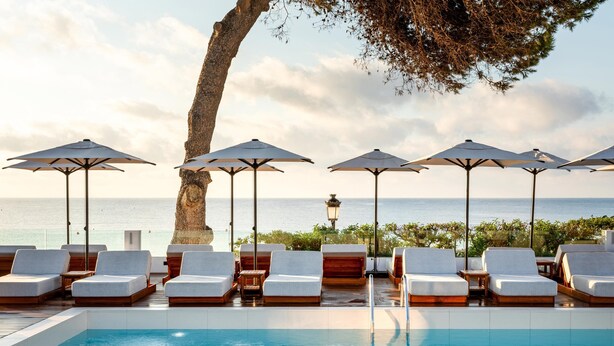 A poolside area with lounge chairs and umbrellas, overlooking the sea. - Hotel Riomar Ibiza, A Tribute Portfolio Hotel (Santa Eulalia del Rio)