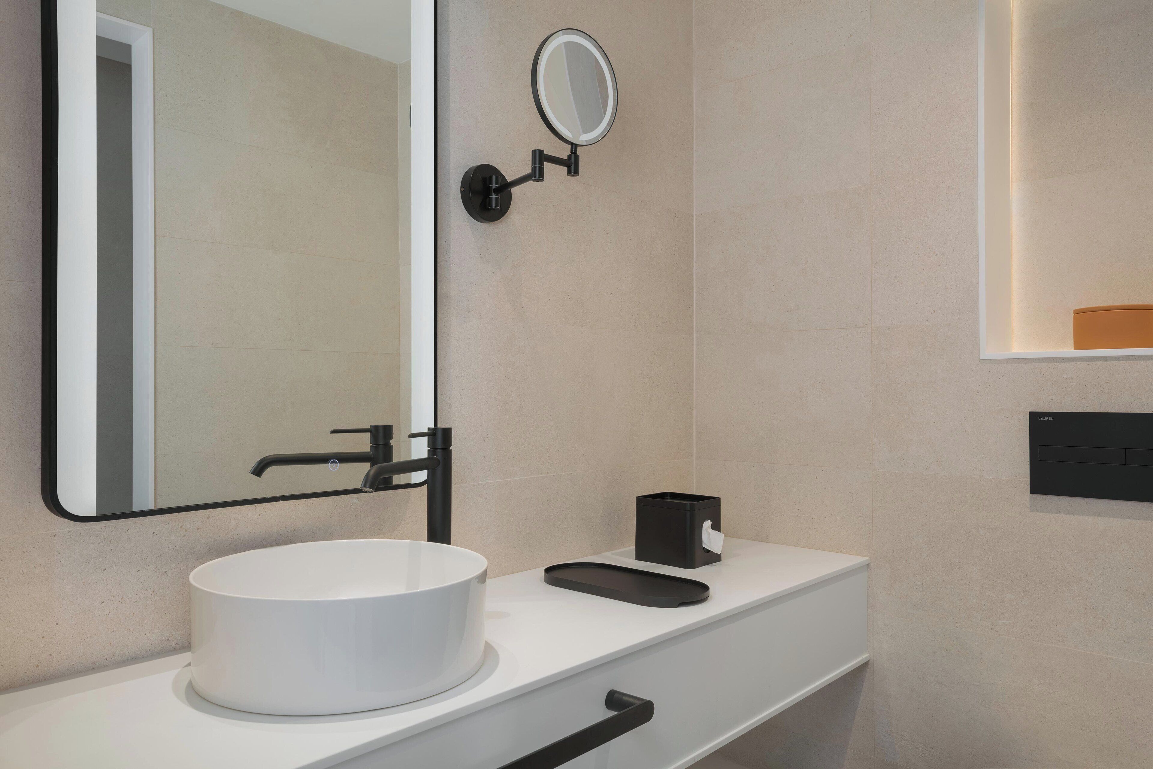 Un baño moderno con un lavabo blanco redondo, un grifo negro, un espejo y un pequeño jabonera negra.